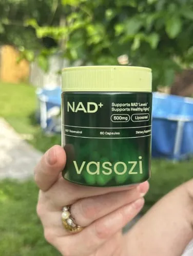Hand holding a bottle of Vasozi NAD+ outdoors in a sunny backyard with a pool in the background